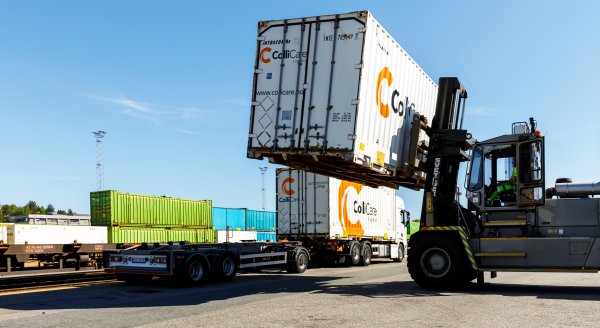 A white container is loaded from a train wagon on to a truck trailer by a forklift.